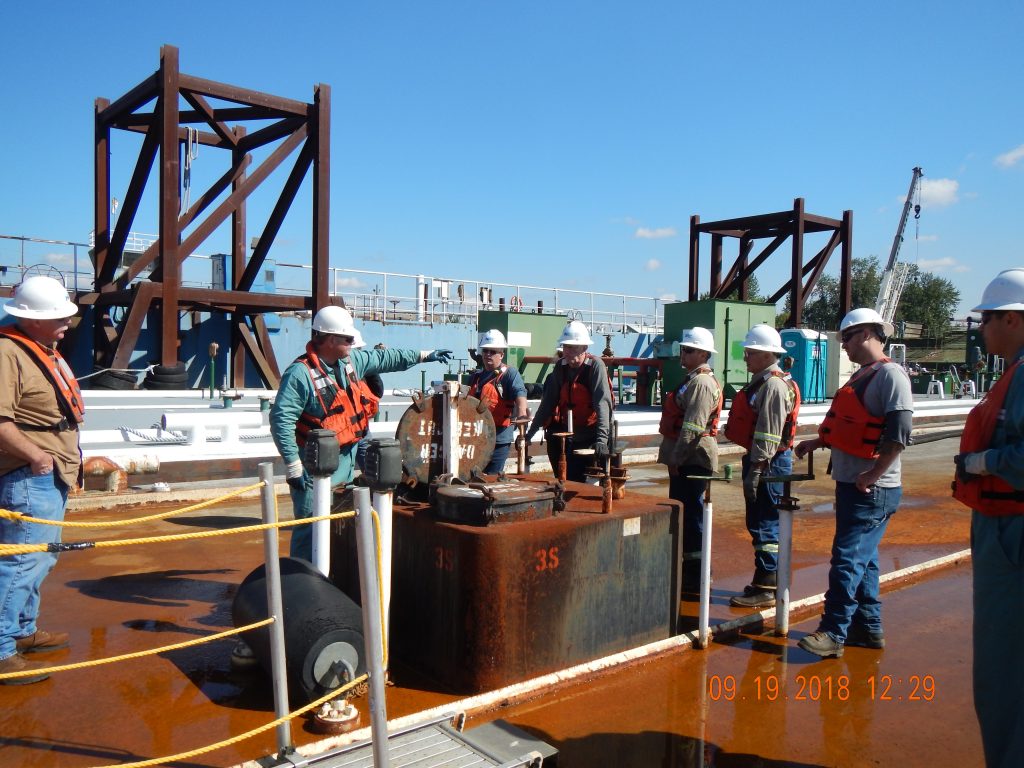 A group stands with hardhats and life vests on a dock going through a contractor training.