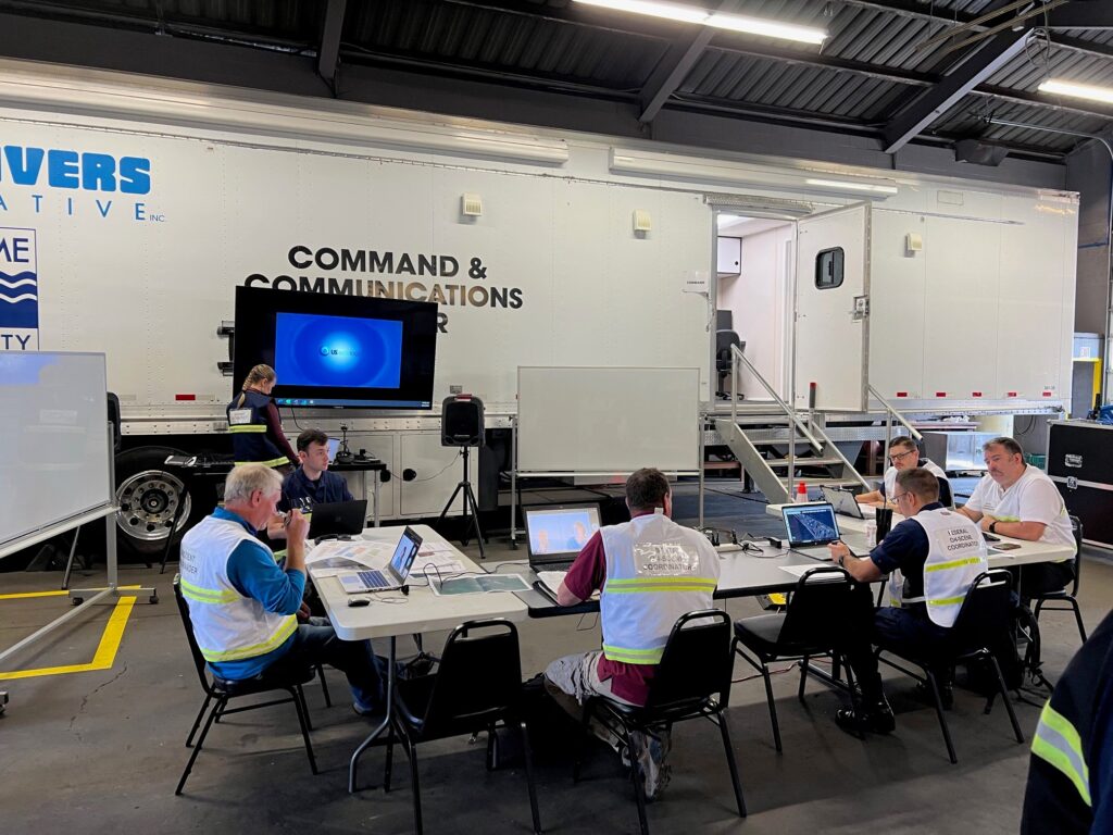 Planning Section Chief setting up for Tactics Meeting at CPBR TTX held at Clean Rivers Cooperative Operations Training Facility Bay 1 utilizing the Mobile Command and Communications trailer. Pictured with Unified Command.
